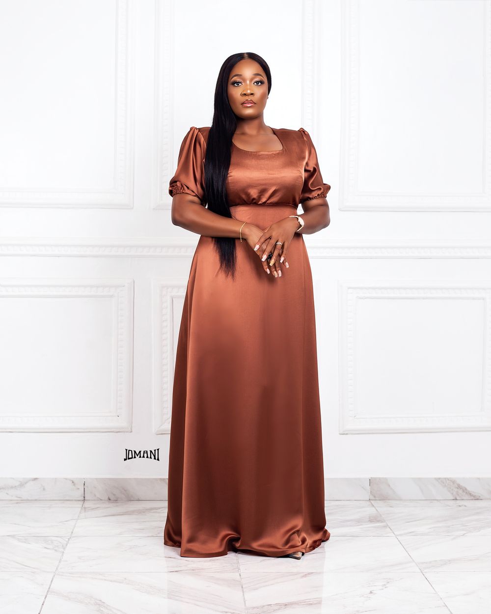 Woman in a copper satin maxi dress with puff sleeves standing against a white wall.
