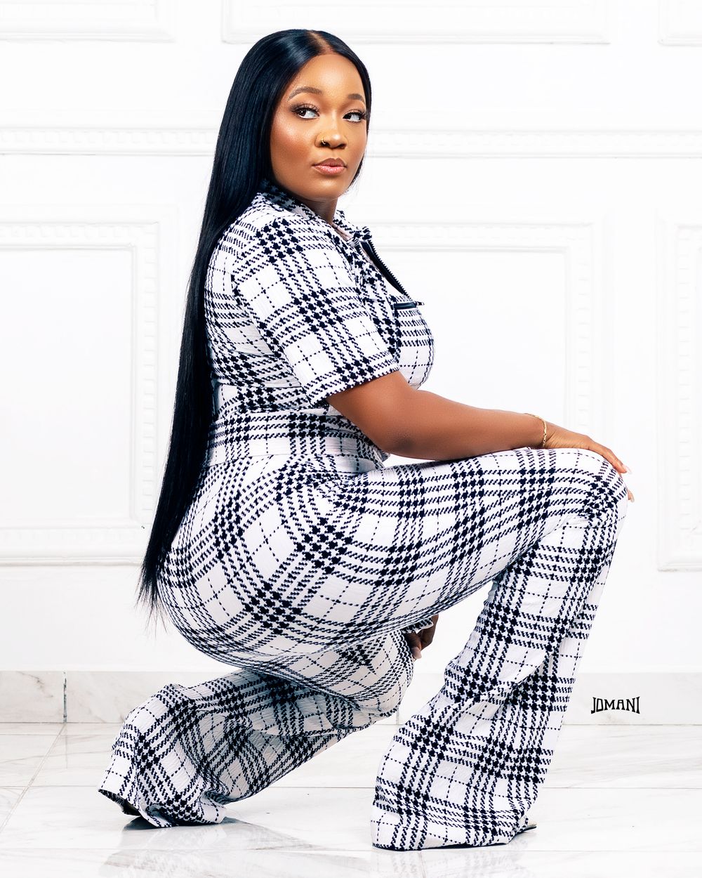 Woman in a black and white plaid jumpsuit posing on a marble floor.
