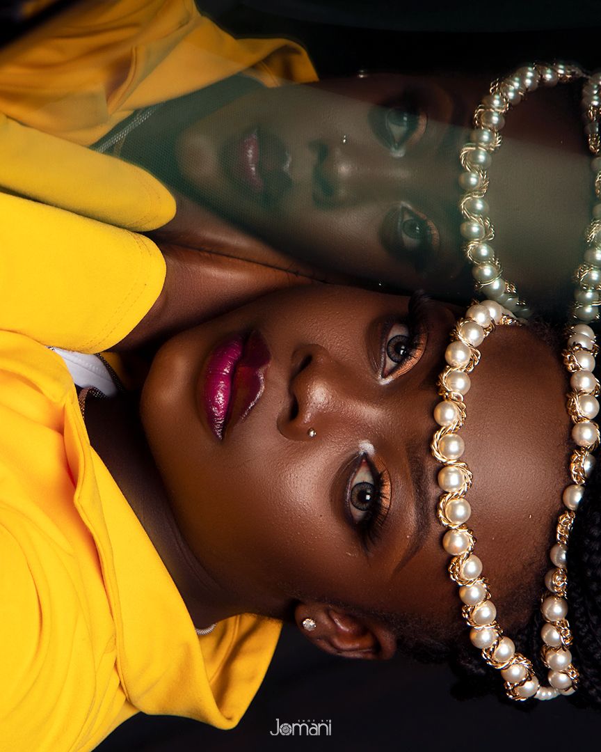 Close-up portrait of woman in yellow with pearl headpiece and pink lips against dark background.