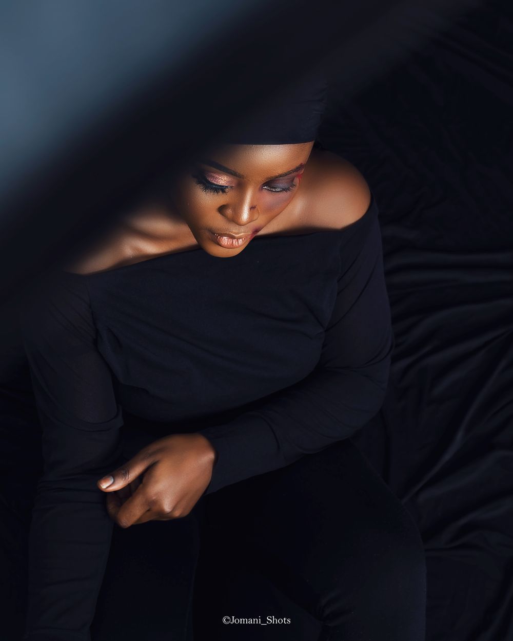 Woman in black long-sleeve top posed dramatically under dark fabric in artistic low-key portrait.