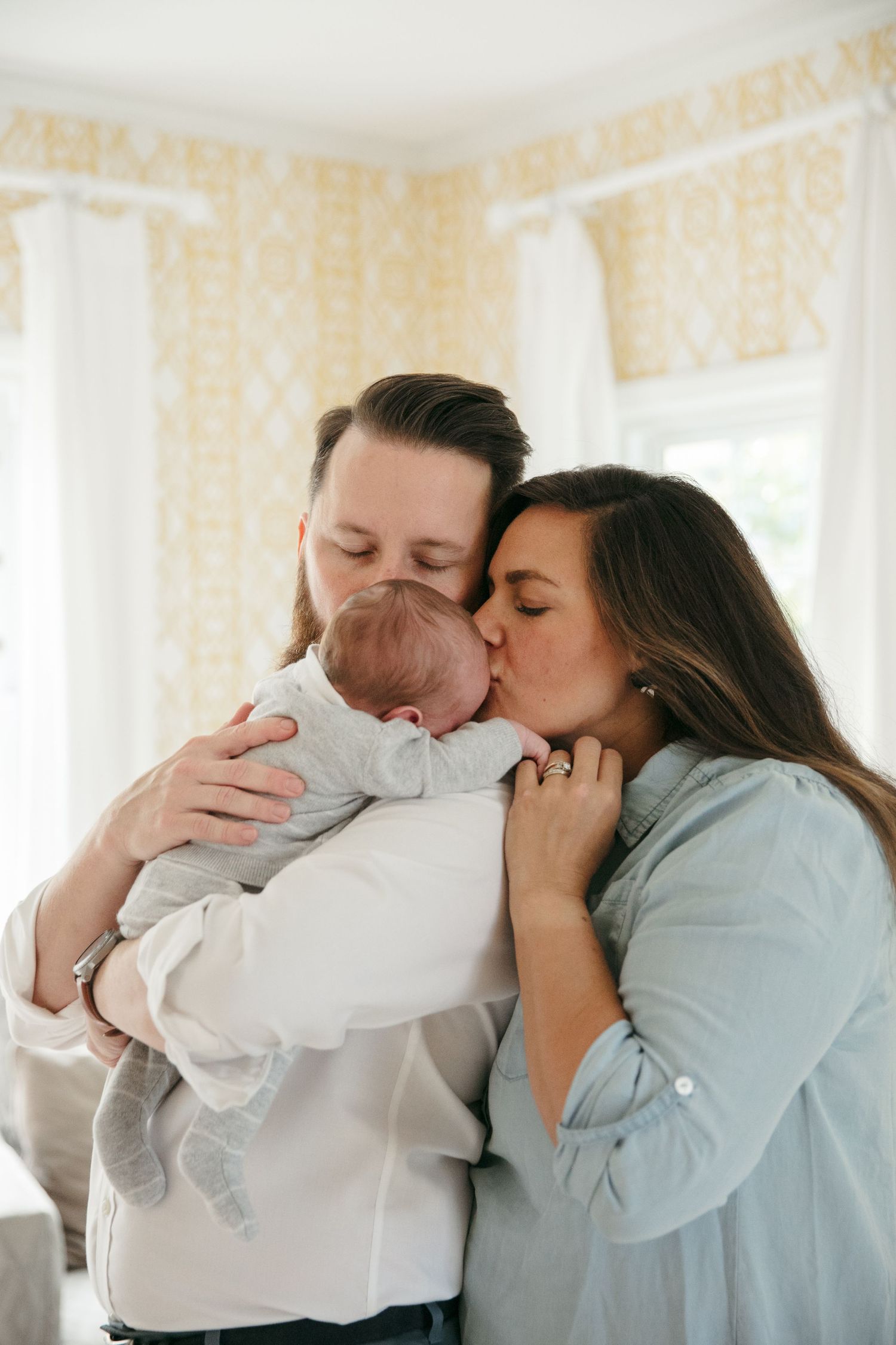 Tender moment with infant in a bright room with floral wallpaper.