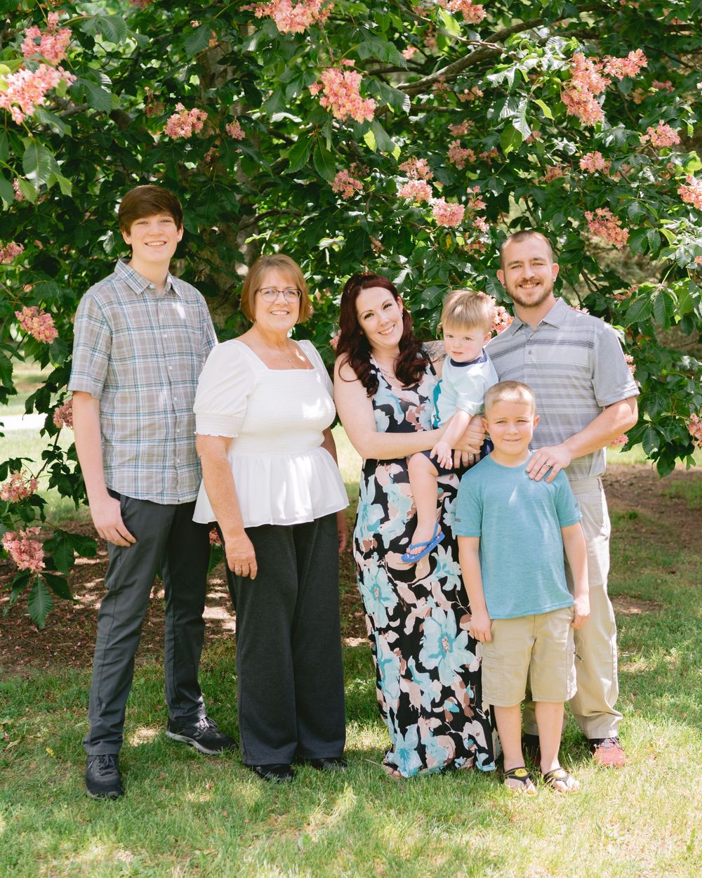 A multi-generational family poses together under flowering trees in summer.