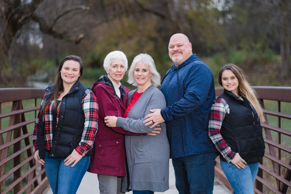 Family group posing together on wooden bridge wearing coordinated blue and plaid outfits.