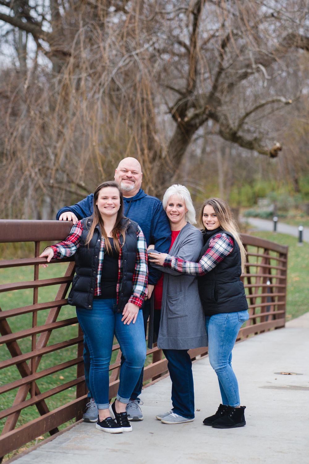 Family members posing playfully on wooden bridge railing in matching casual outfits.