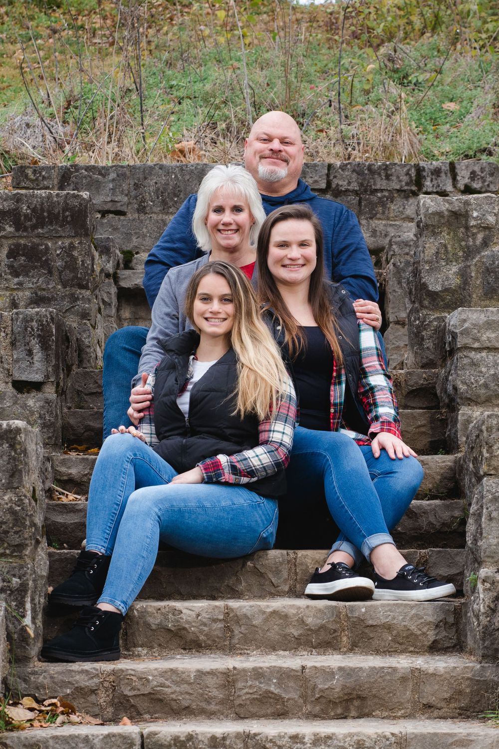 Family sitting together on stone steps outdoors wearing coordinated blue and plaid clothing.
