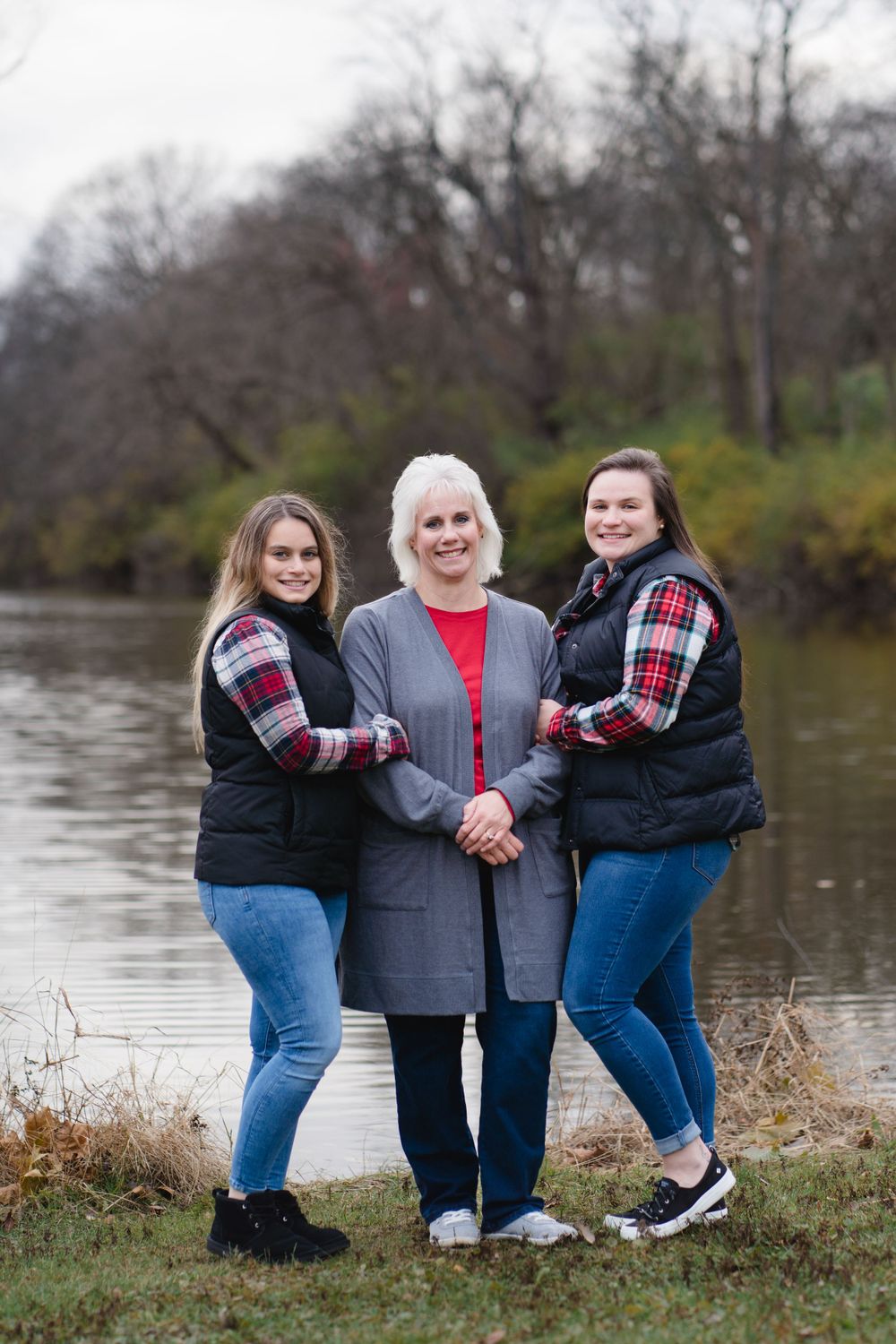 Family group posing casually by lake wearing coordinated outfits in blue and plaid.