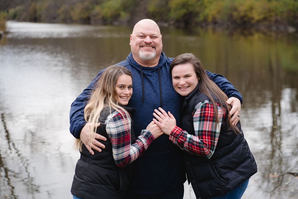 Family members hugging and laughing together by lake during photo session.