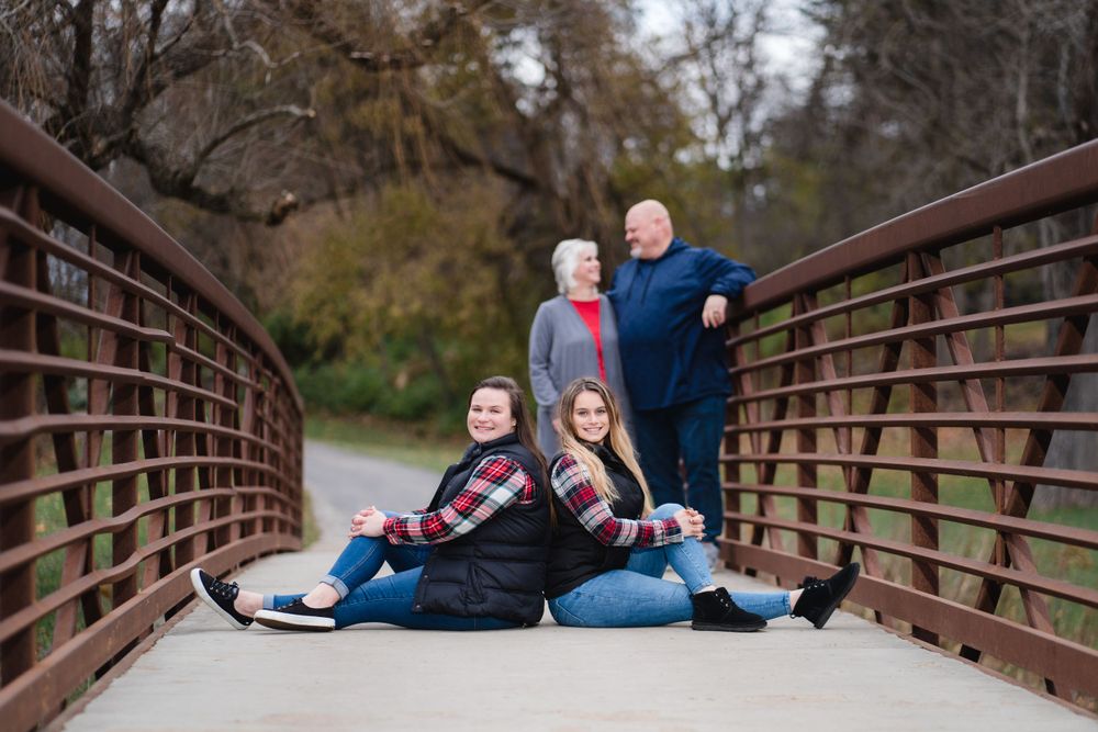 Family group sitting together on rustic wooden bridge during outdoor photoshoot.