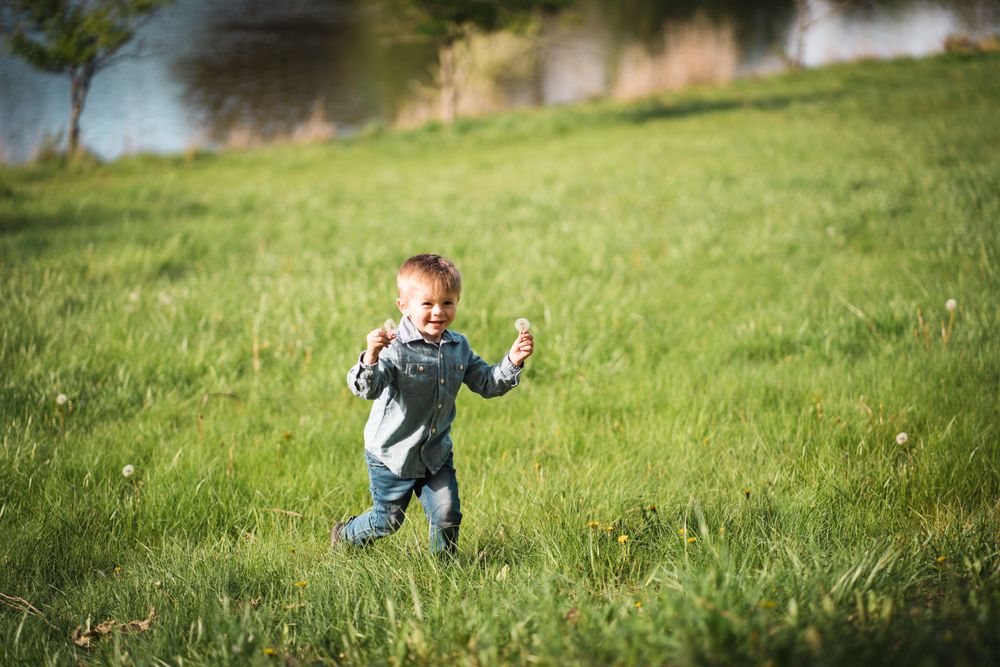 A toddler runs joyfully through a grassy field on a sunny day.