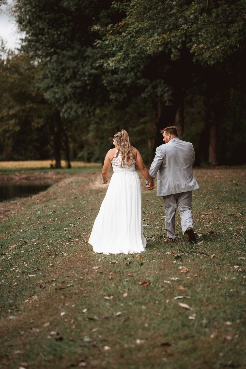 Newlyweds walk together on a grassy path through an autumn park.