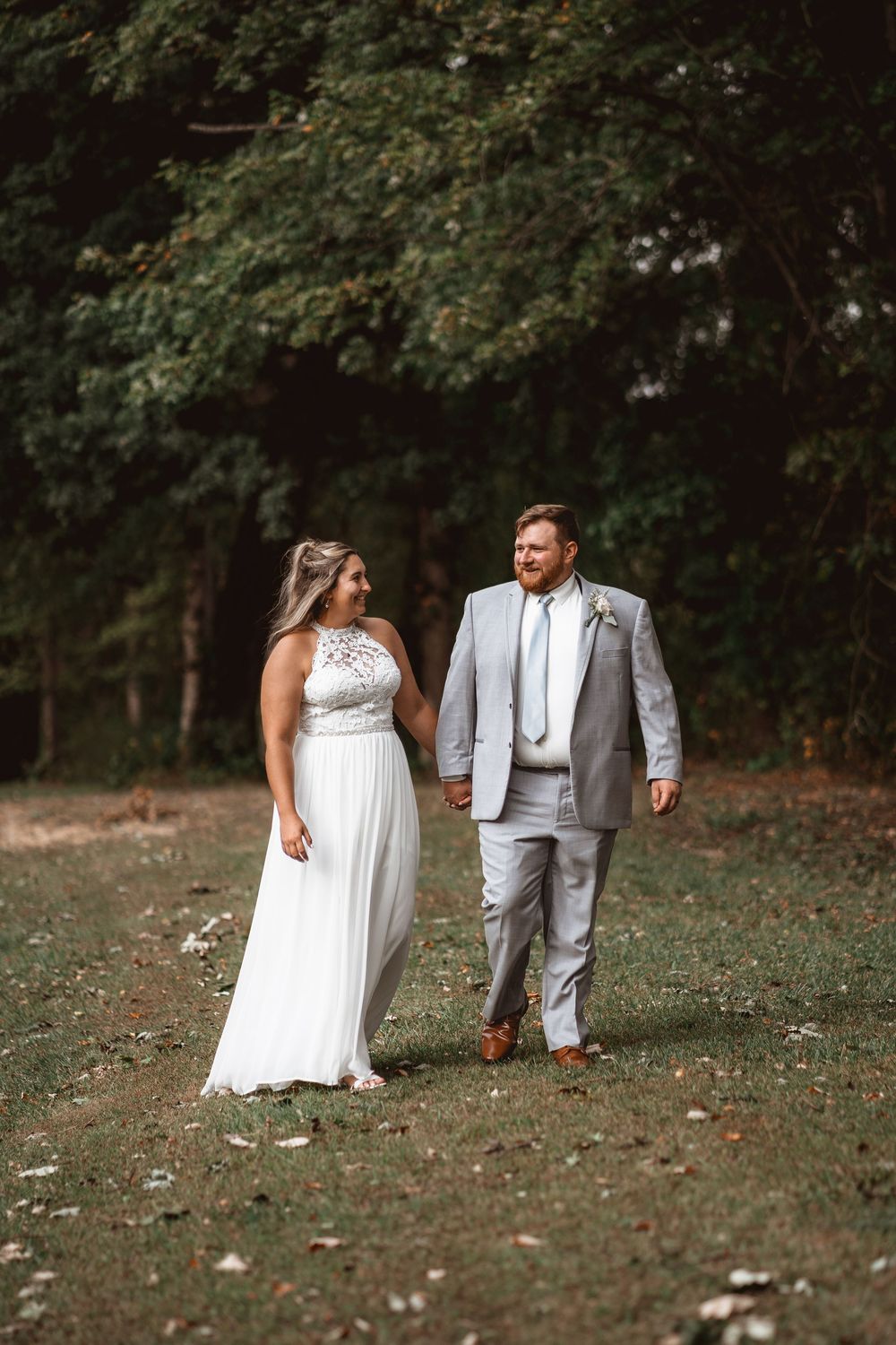 A couple in wedding attire shares a loving glance while walking through a park.