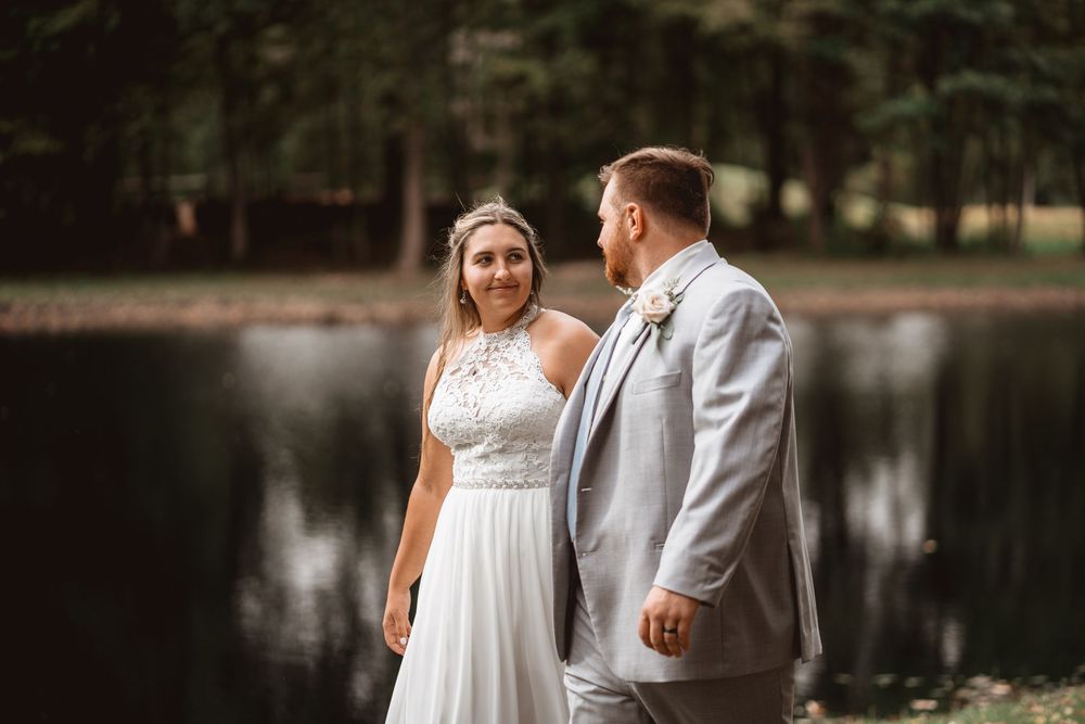 A couple in wedding attire poses by a serene lake during their autumn wedding.