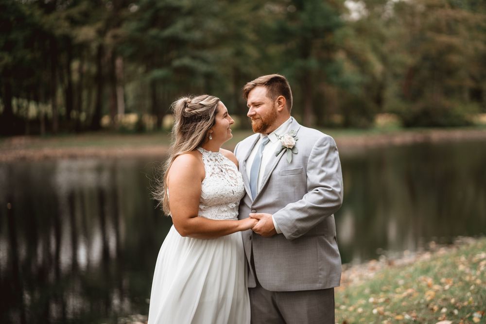 A romantic outdoor wedding ceremony by a serene lake with white chairs and floral decorations.