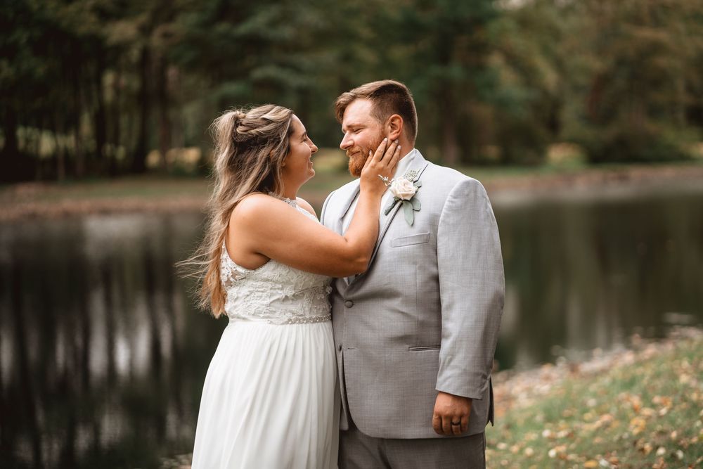 A beautiful lakeside wedding ceremony with guests seated on white chairs under tall trees.