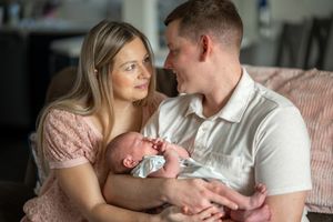 Parents in soft pink and white clothing tenderly hold their newborn baby in an intimate indoor setting.