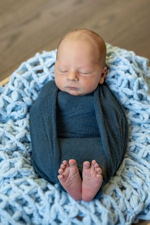 A sleeping newborn baby swaddled in navy blue on a chunky knit white blanket shown from different angles.