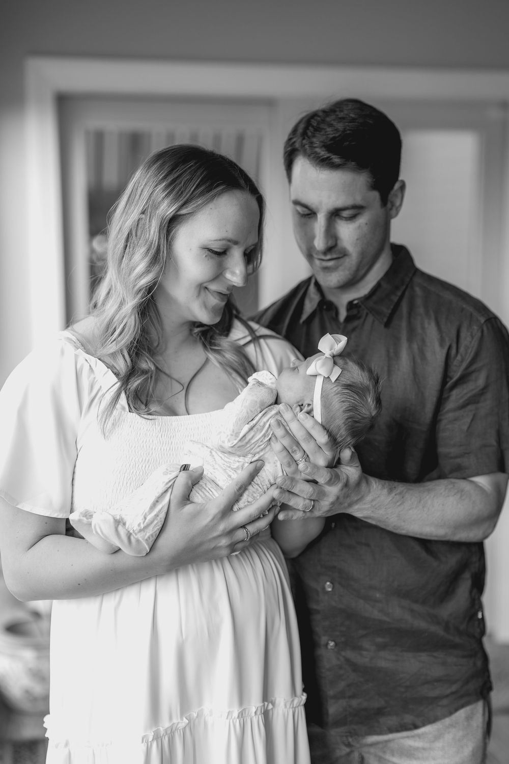 Black and white photo series showing tender moments between parents and their newborn baby at home.