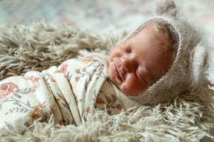A sleeping newborn wearing a knit cap rests peacefully on soft white shag material.