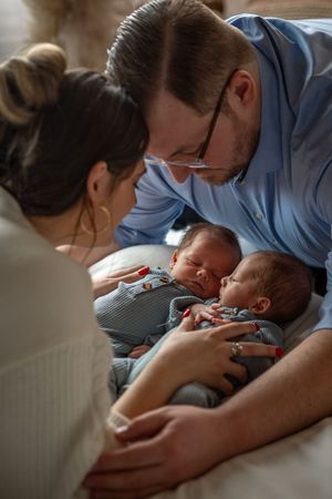 Parents lovingly gaze at their sleeping twin babies dressed in matching striped outfits.