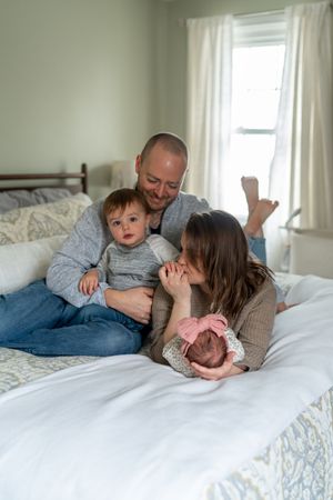 Family sharing tender moments together while relaxing on white bedding with floral patterns.