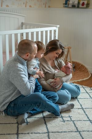 Family members sitting together on a patterned carpet while looking at a mobile device in a cozy home setting.