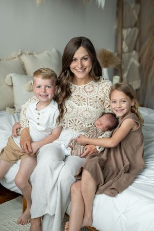 Family portrait series showing siblings and newborn baby relaxing together on white bedding in matching outfits.