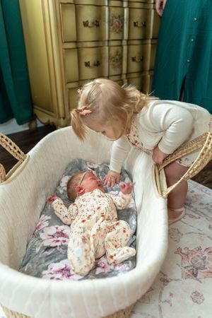 A sequence of photos showing a toddler and baby lying together in a cozy white cushioned chair with floral patterns.