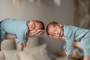 Newborn twins in light blue outfits sleeping peacefully on a white textured blanket.