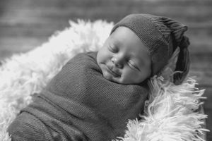 A sleeping baby rests peacefully on soft white fur while wearing a gray knit sweater.