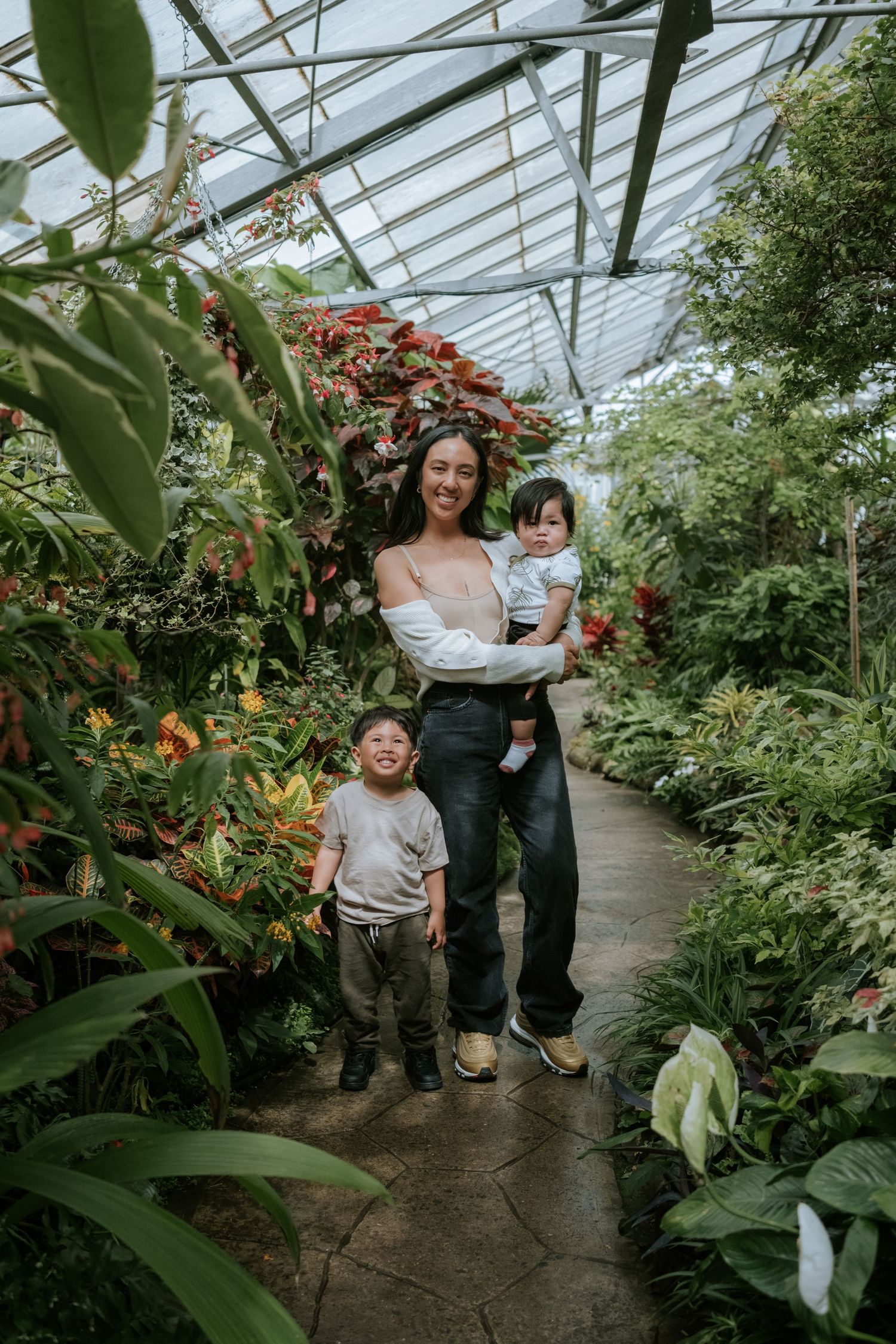 A family enjoying time together in a lush greenhouse filled with tropical plants and flowers.