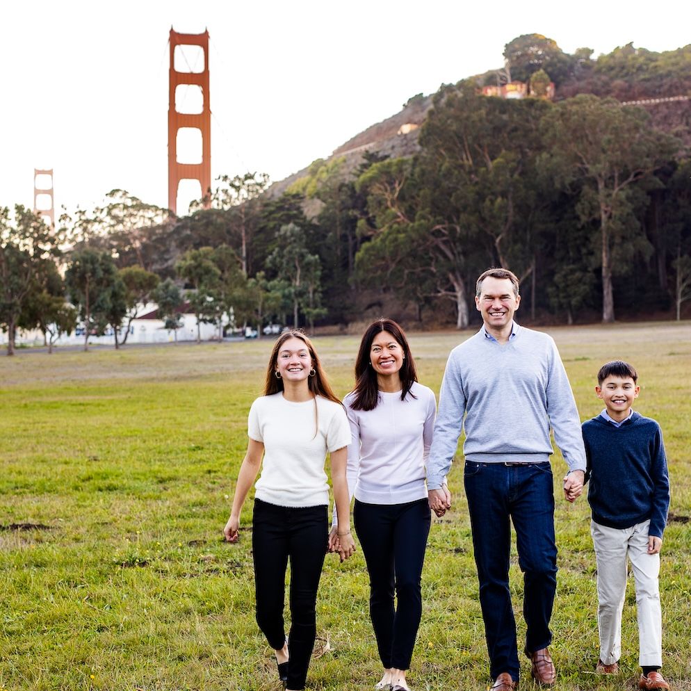 Family of four walking on grass with the Golden Gate Bridge in the background on a clear day.
