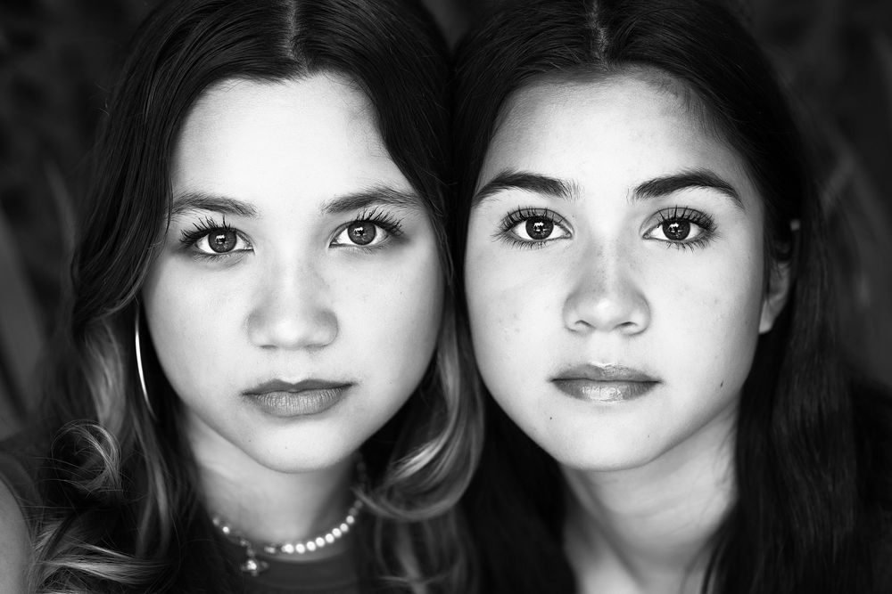 Black and white portrait of two young women with similar features posing closely together, looking directly at the camera.