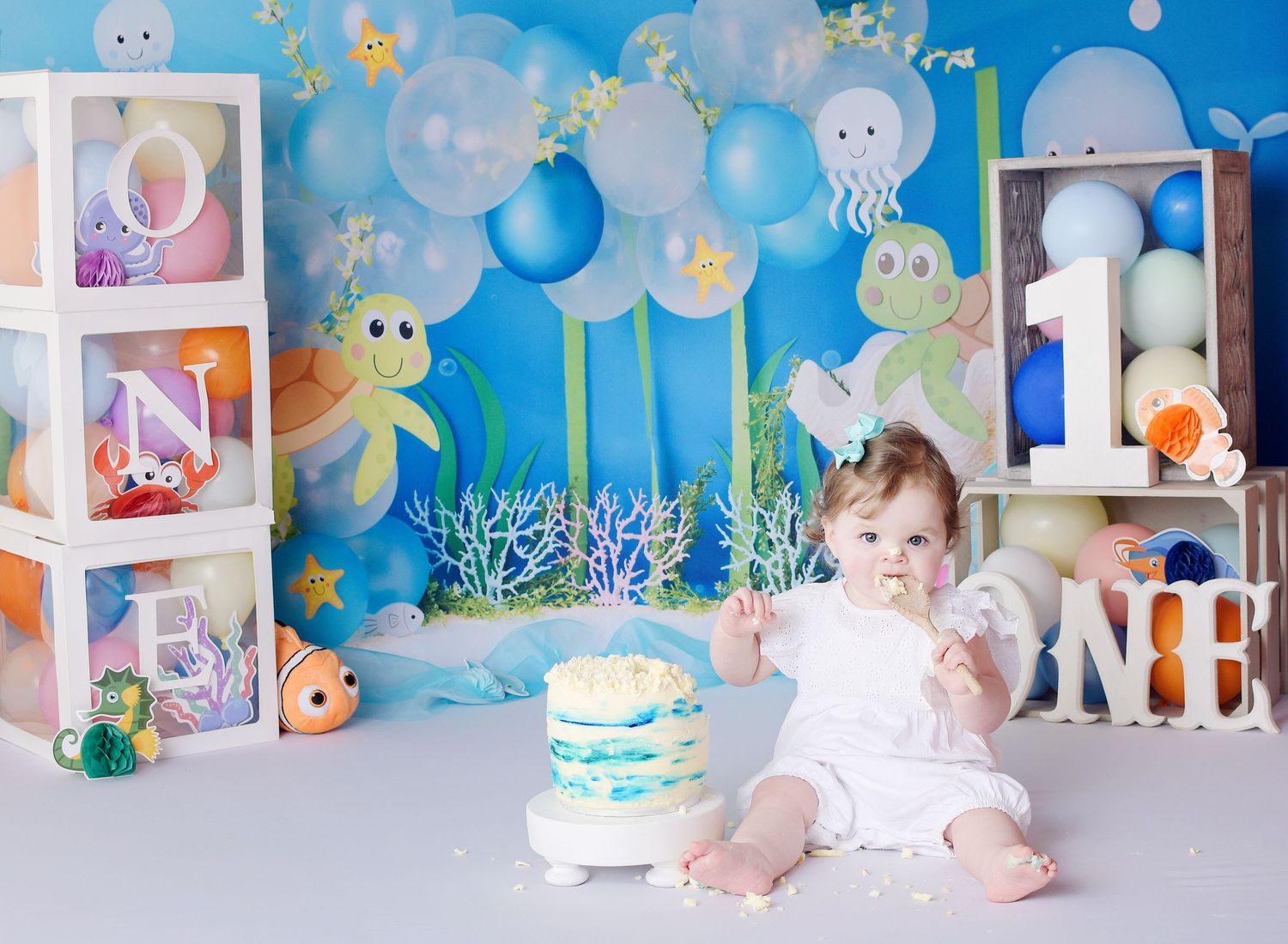 Cake smash first birthday session. Underwater turtle theme with yummy, squidgy cake. The child eats the cake off of the spoon.