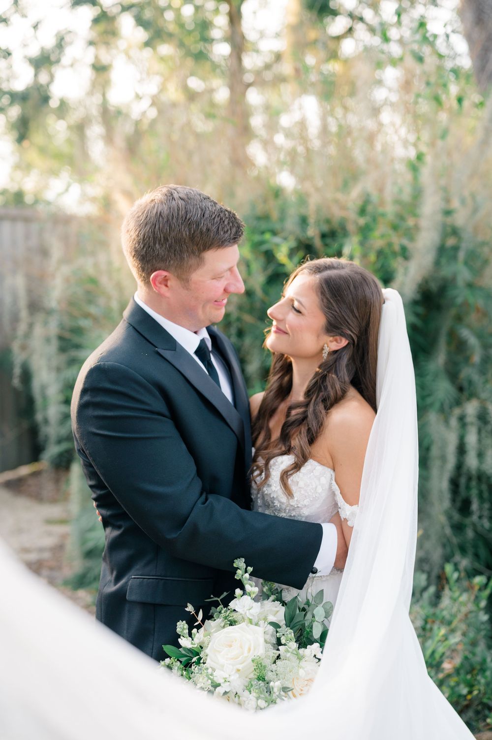 A romantic wedding couple shares intimate moments in a sunlit outdoor setting with natural greenery.