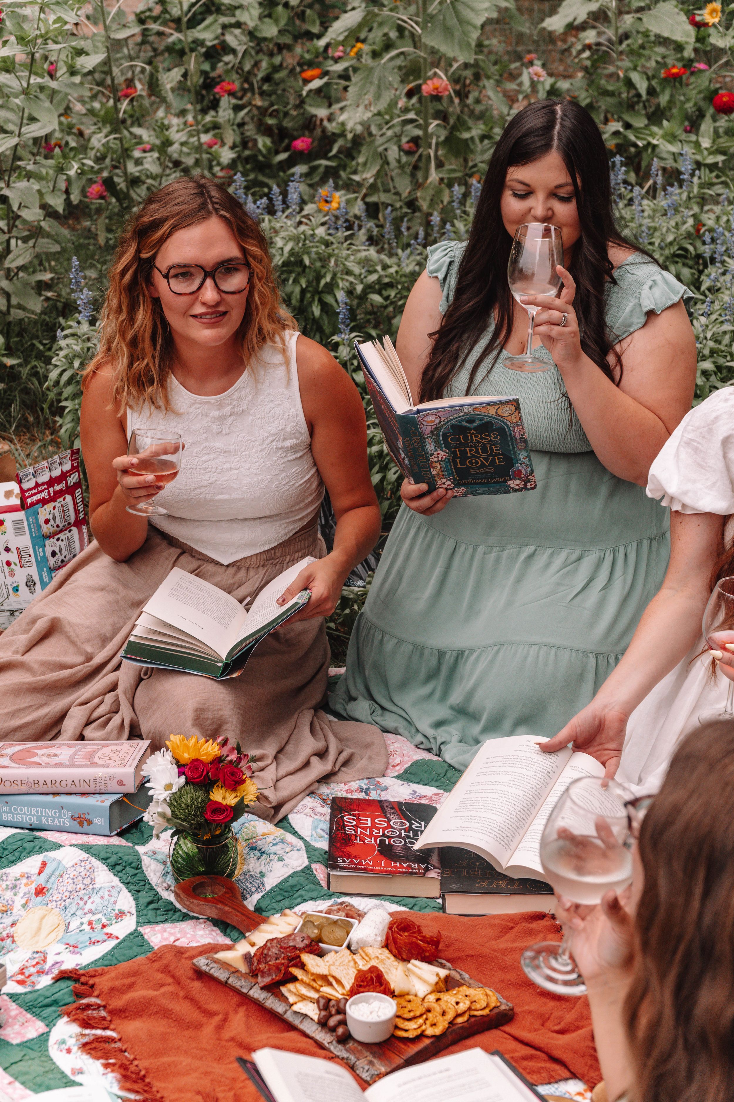 Friends enjoying a picnic with books and snacks on a patterned blanket.