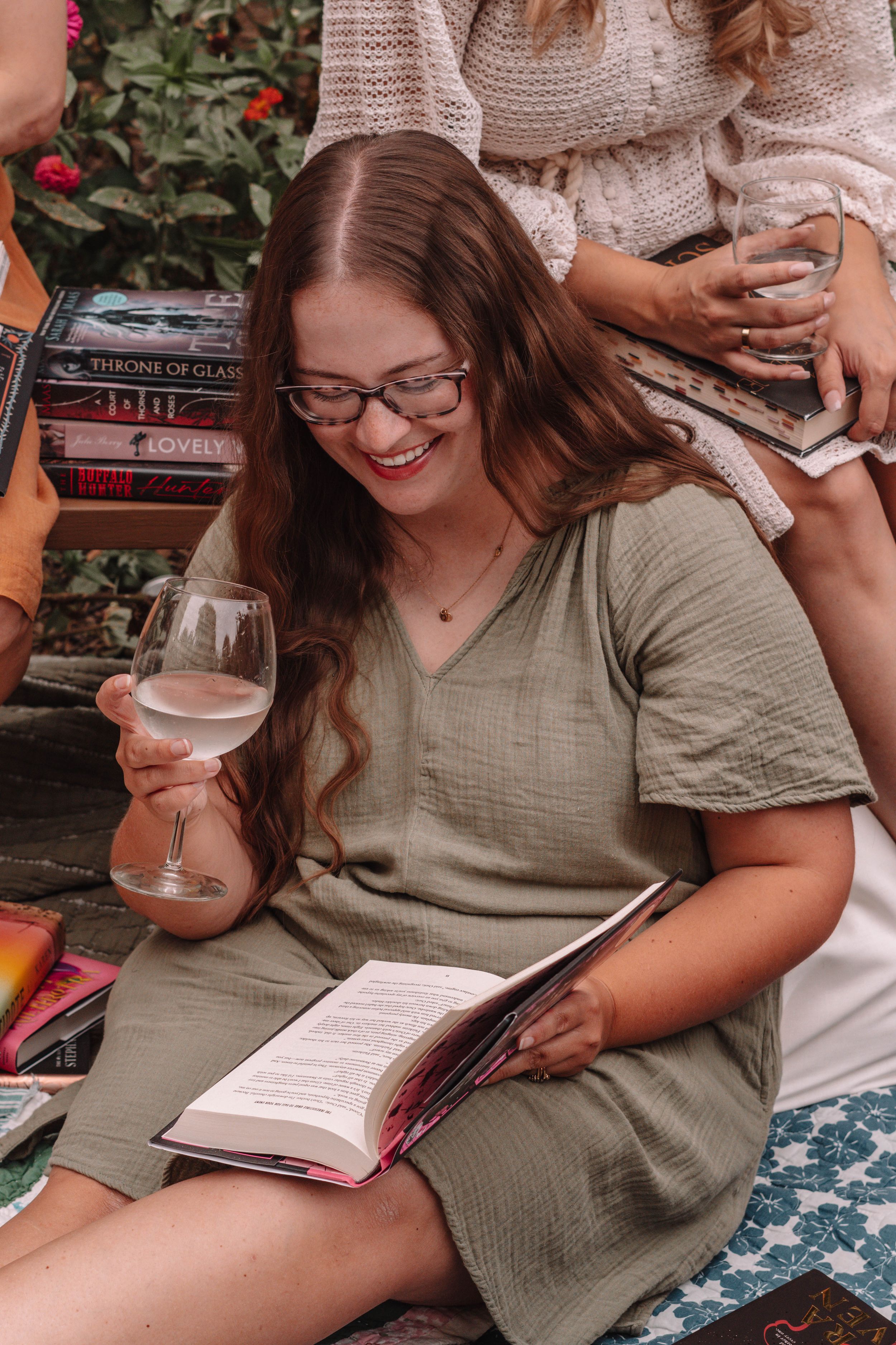 Women reading books while relaxing on blankets in a garden setting.