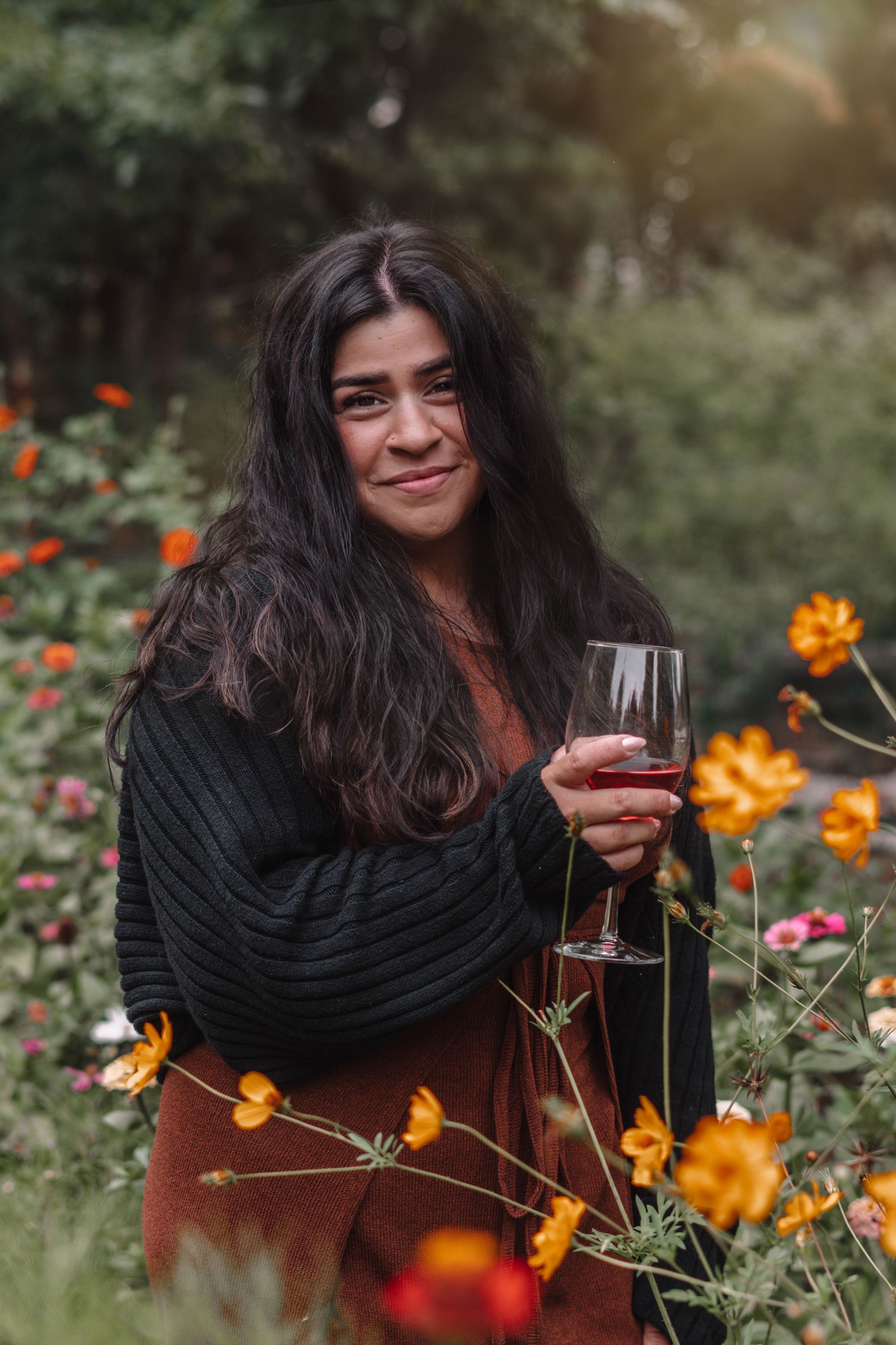 Woman in black wrap enjoying wine among blooming orange flowers in garden.