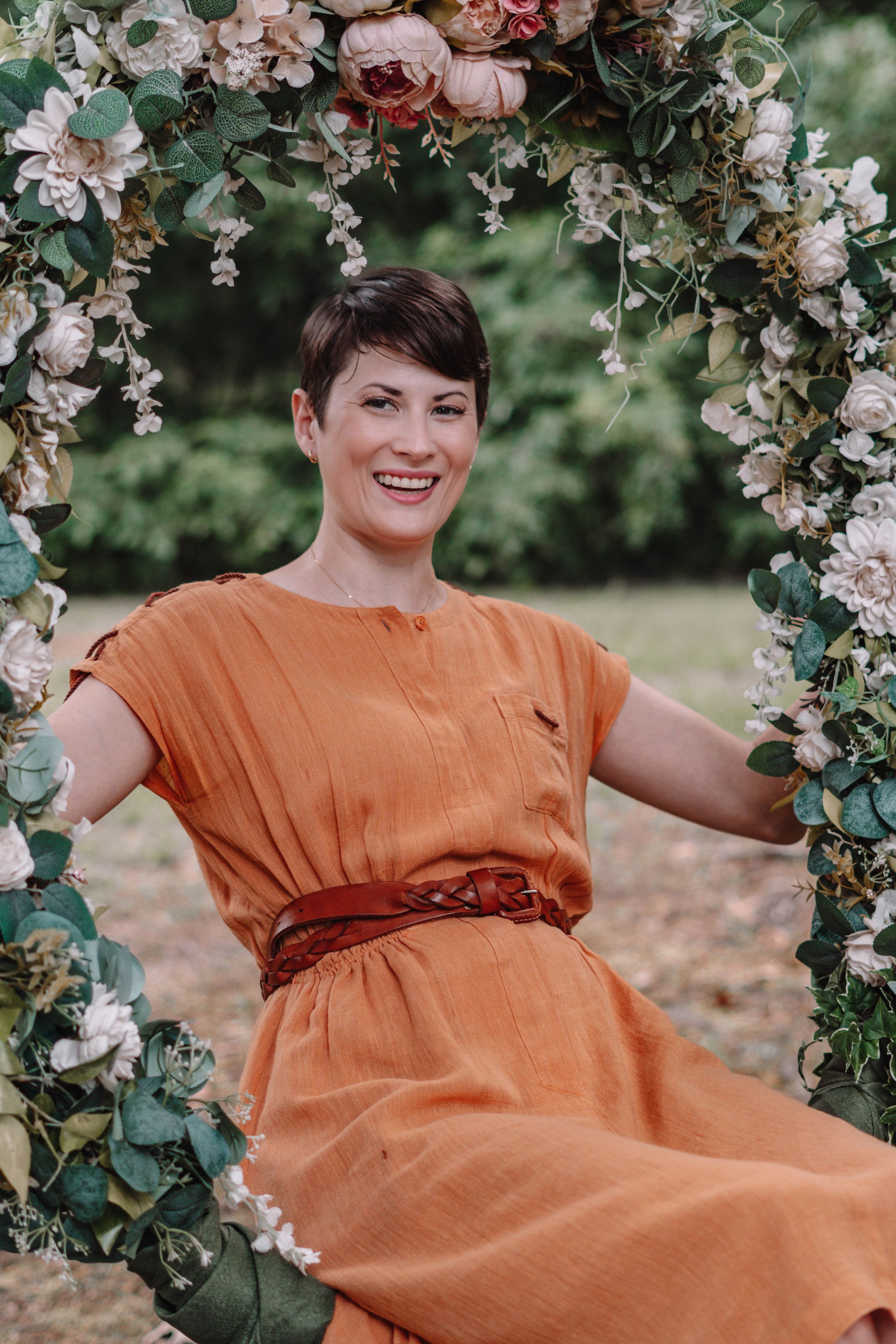 Person in orange dress relaxing on floral swing in garden setting.