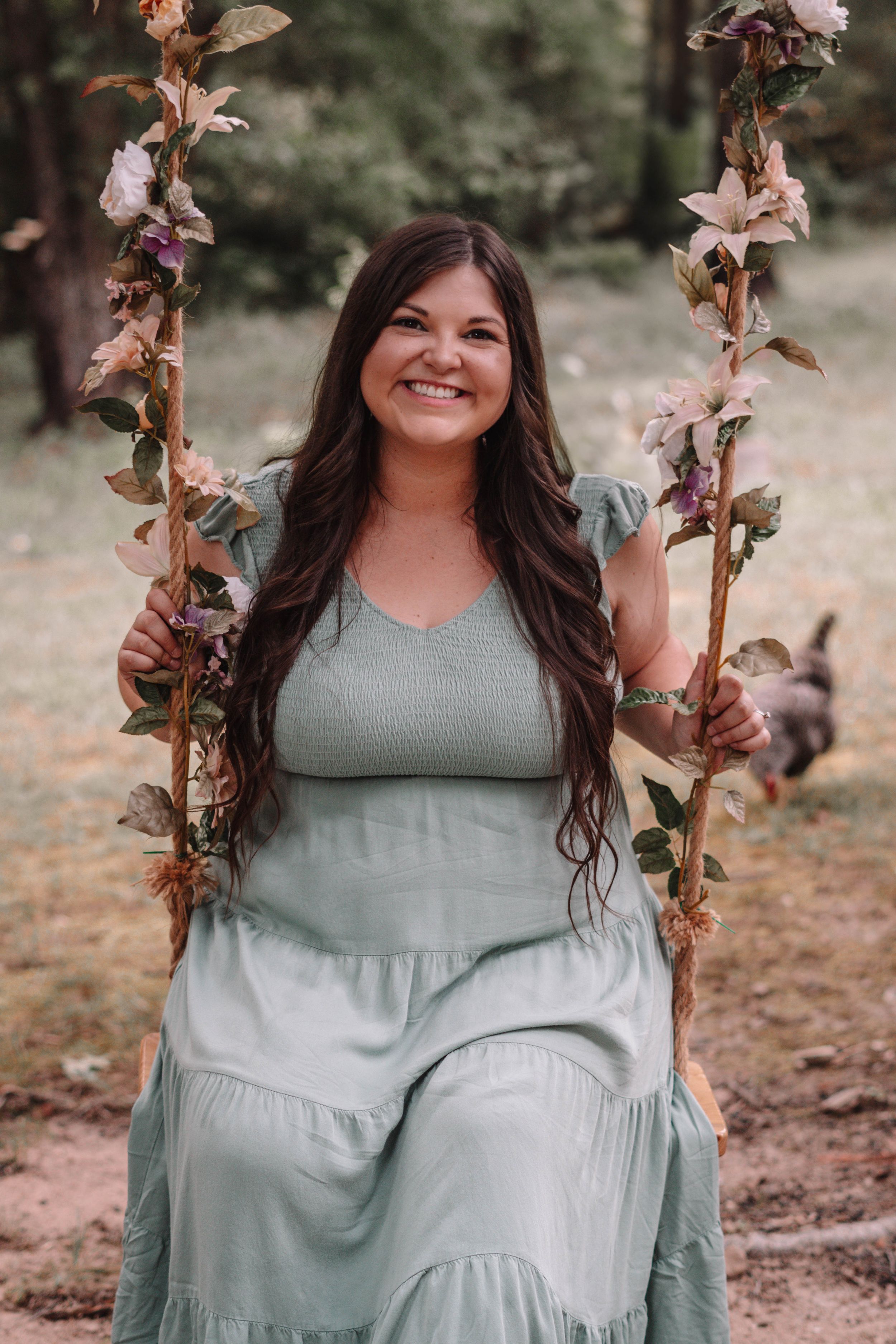 Person in sage green dress posing with floral garden backdrop.