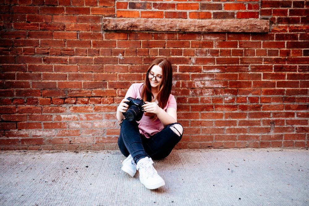 Senior girl sitting against brick wall smiling at her camera in Dickson, TN