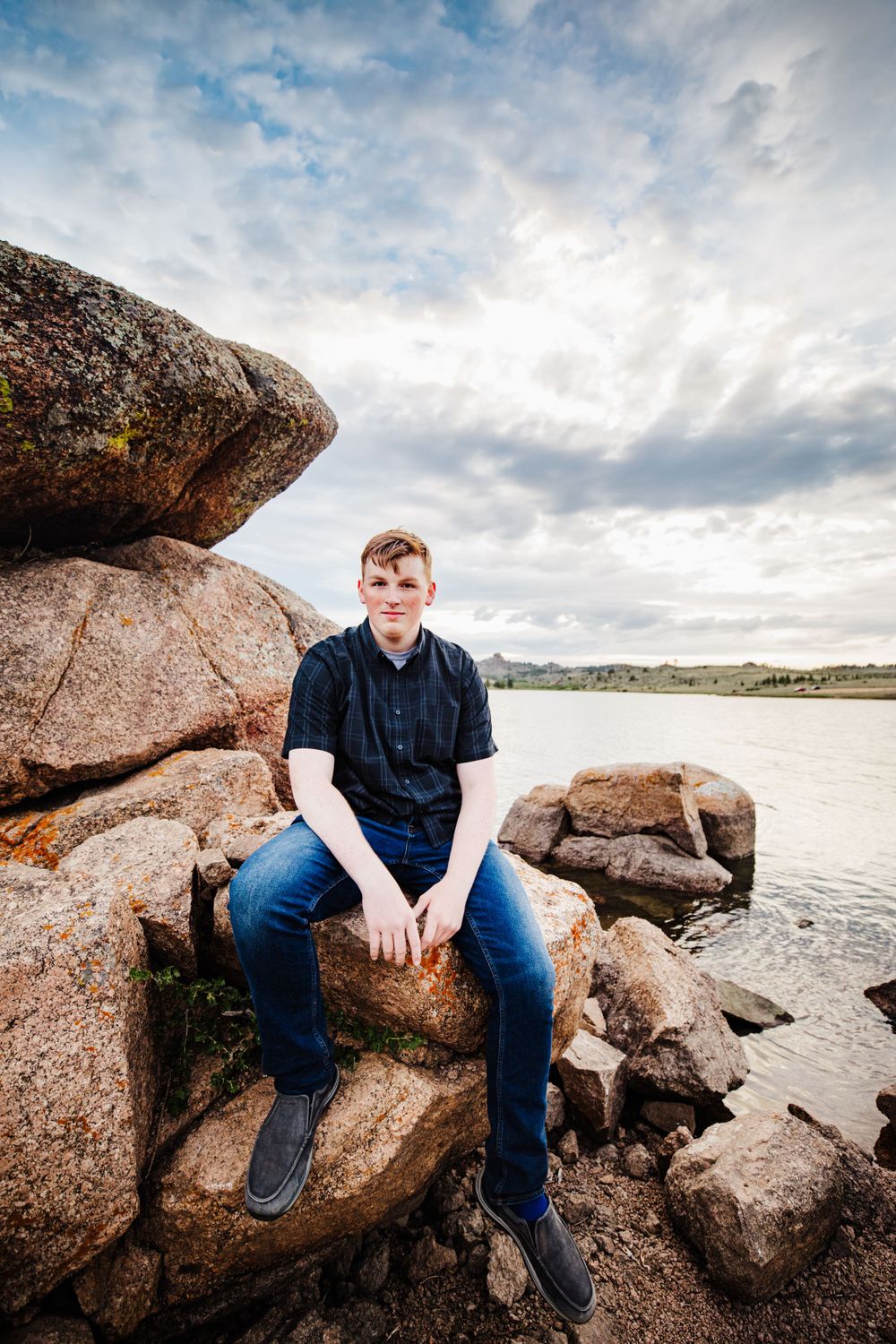 Senior boy sits on rock at the lake and smiles in Dickson, TN