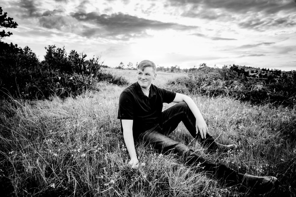 Senior boy smiles in field with cloudy sky in the background in Dickson, TN
