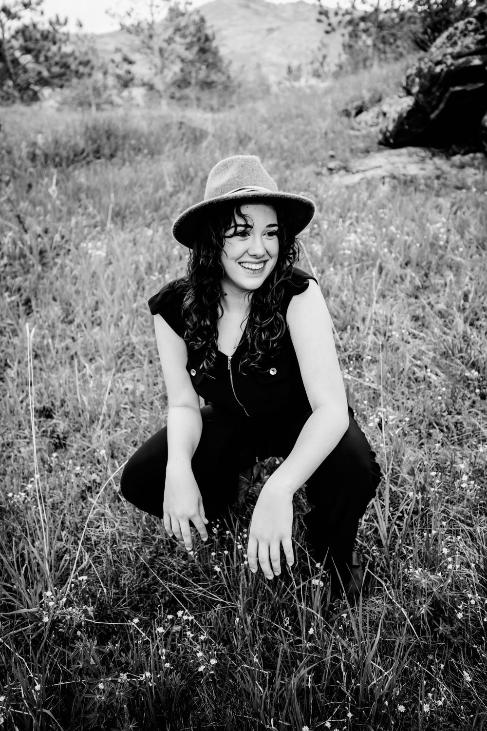 Senior girl in black jumper and a hat sits in field and smiles in Dickson, TN