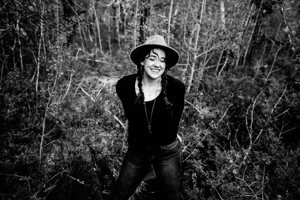 Senior girl in black and a hat smiles in the trees in Dickson, TN