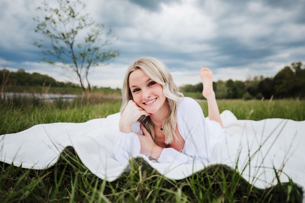 Senior girl on a white blanket in front of lake with beautiful cloud filled sky in Dickson, TN