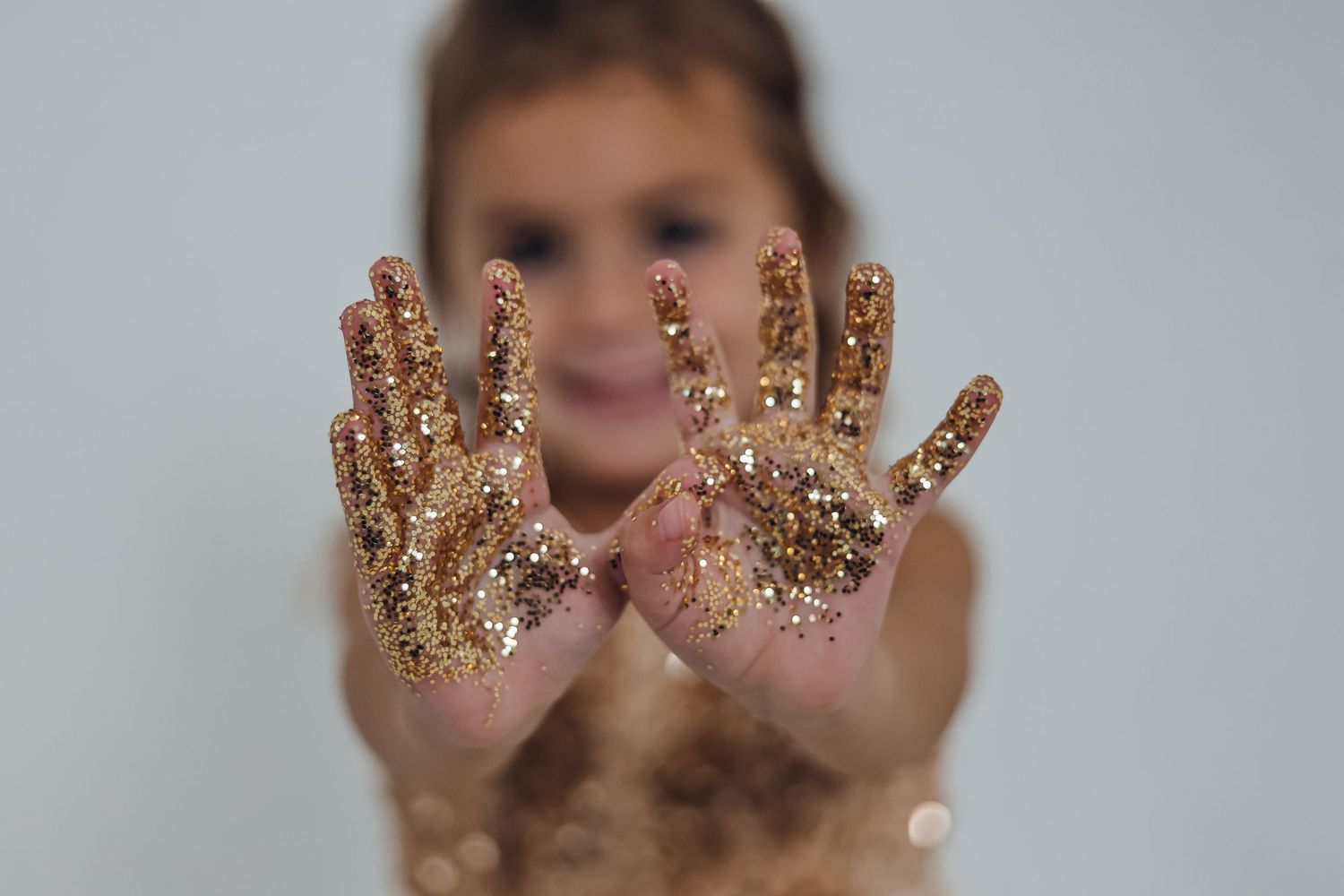 Hands covered in gold glitter sparkle against a light background. Custom photography