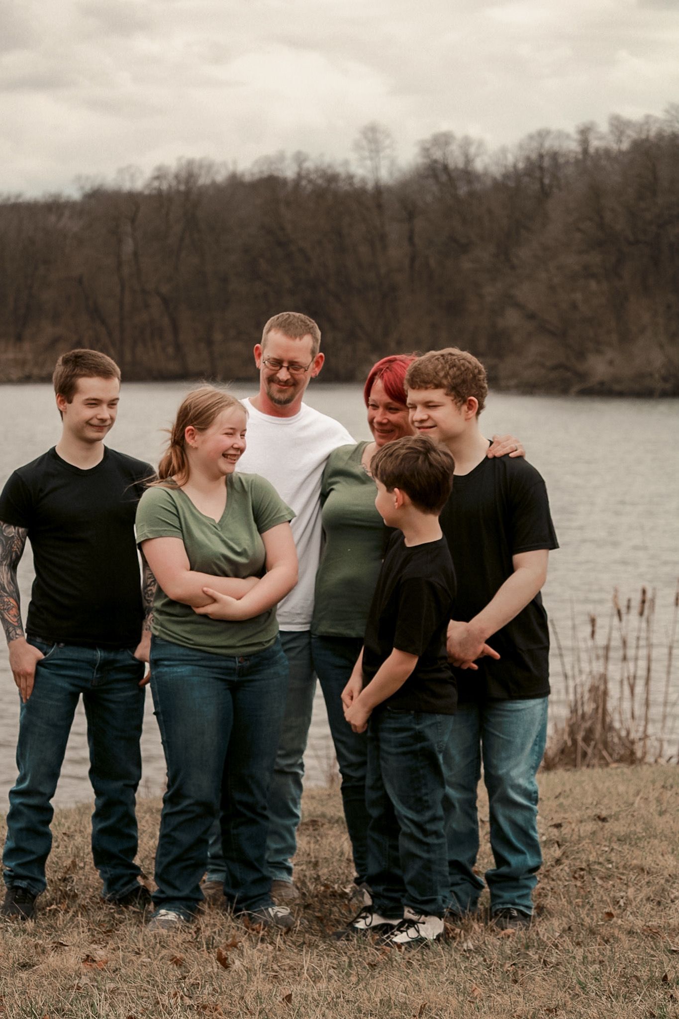 Group stands together by a lake shore during an overcast day.