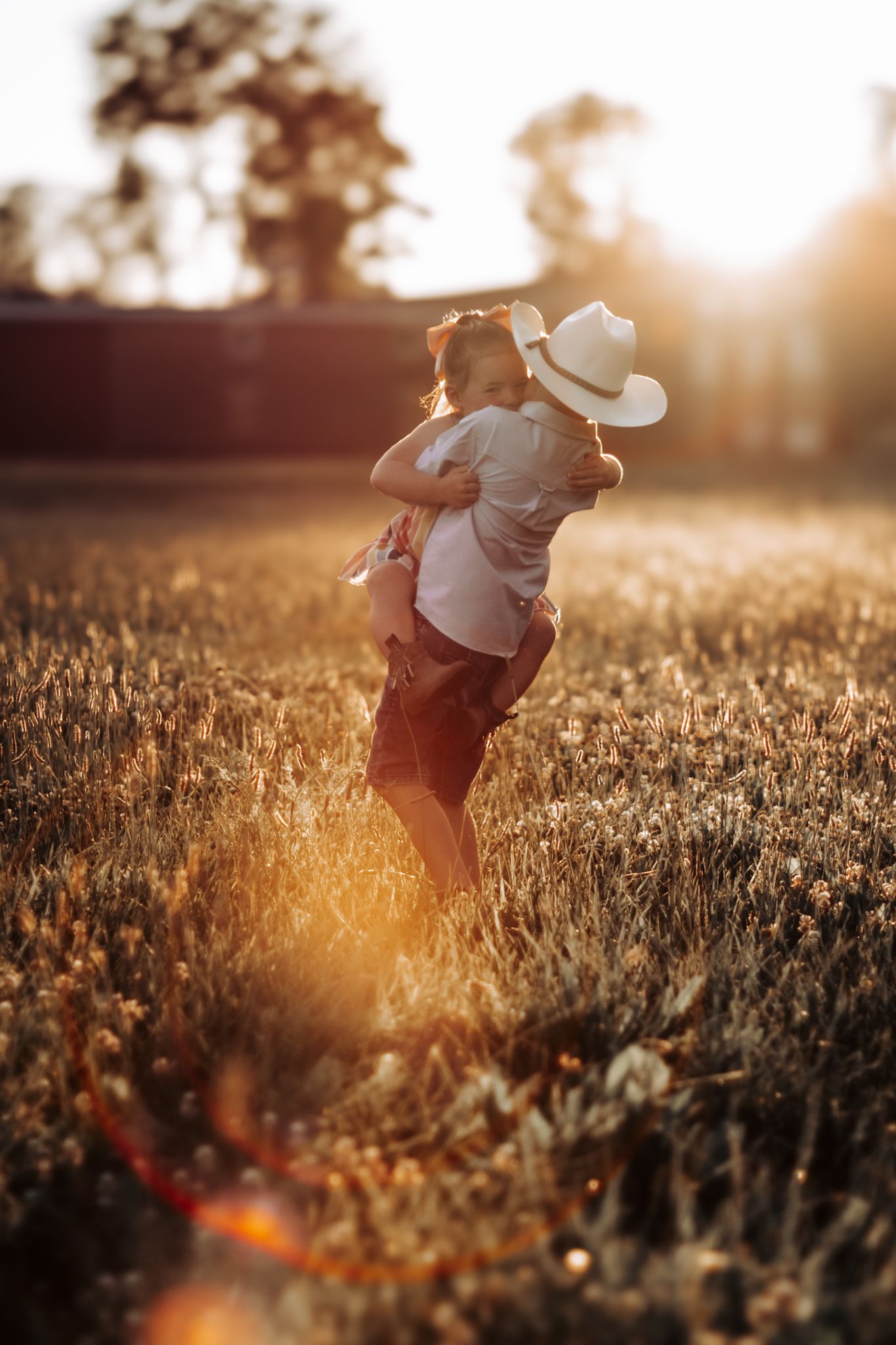 Young figures playing in a golden meadow at sunset with dreamy backlit atmosphere.