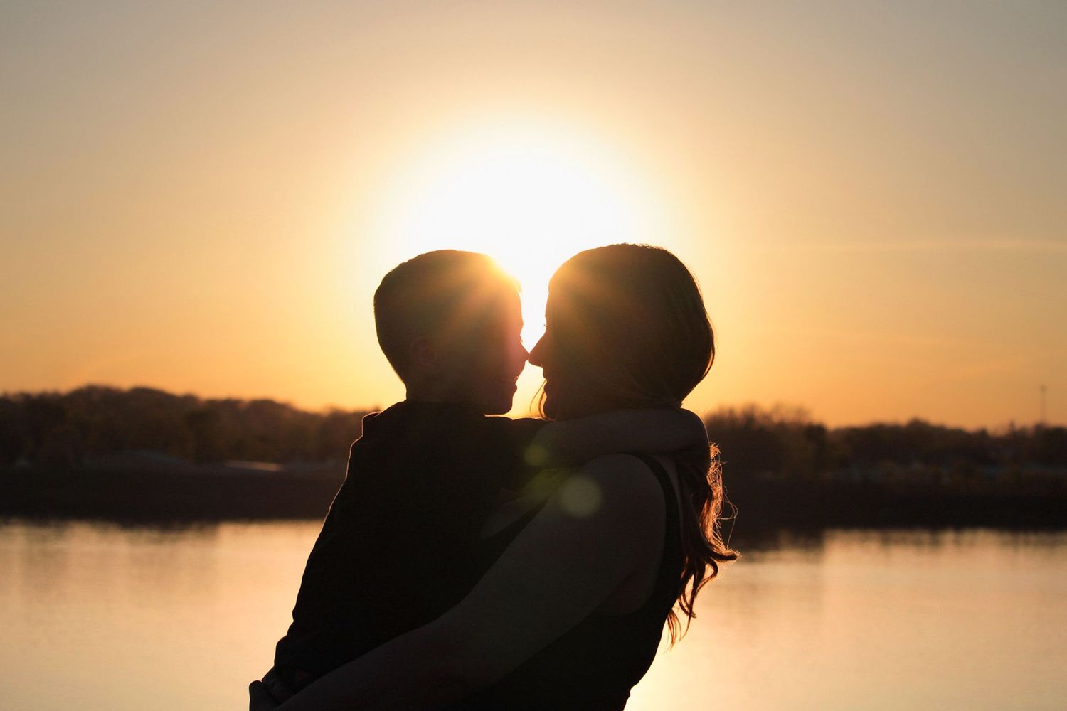Dramatic silhouette of couple against vibrant orange sunset over water.