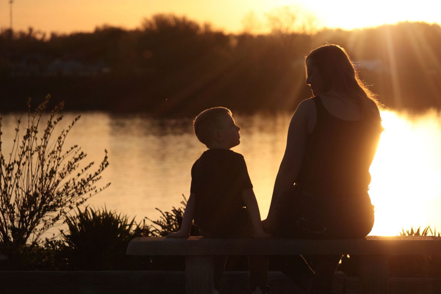 Silhouettes of people sitting by lake during golden sunset.